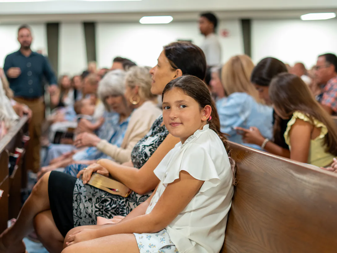 A girl smiling from the pew during a Sunday service at Christchurch Miami, the sanctuary full behind her
