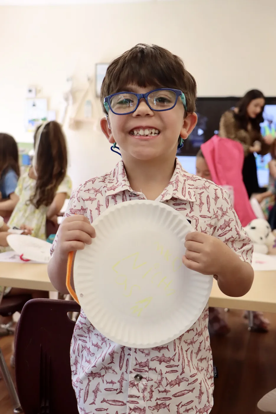 A boy in blue glasses holding up the paper plate craft he just finished
