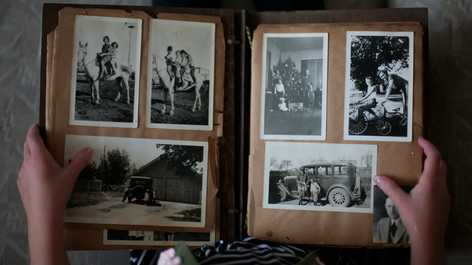 Two hands holding open an old photograph album filled with black and white family pictures