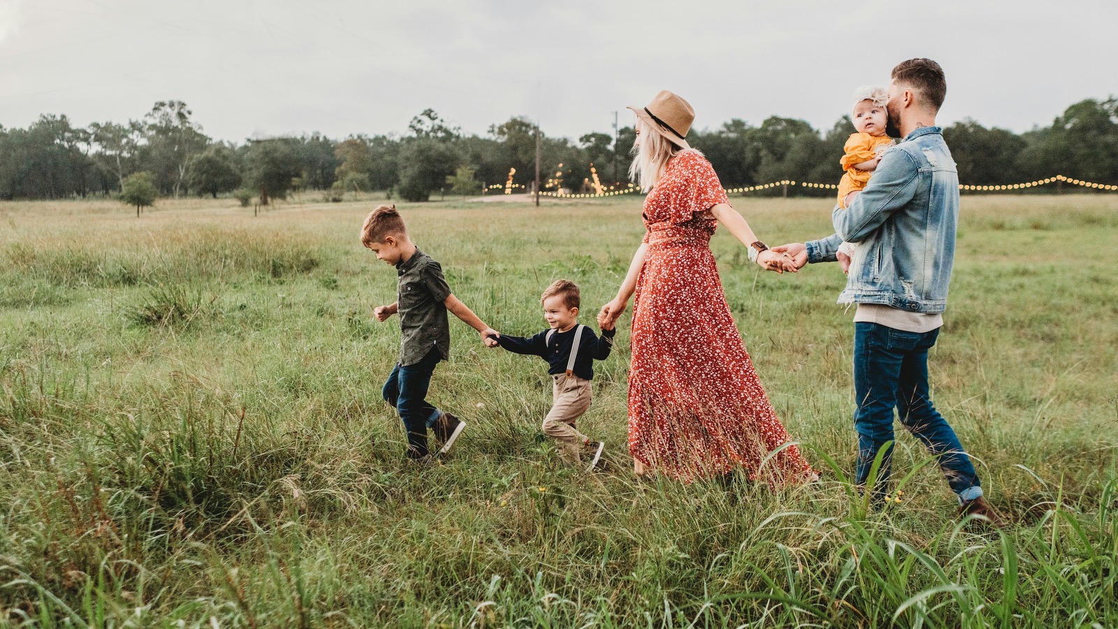 A young family walking through a field holding hands, the father carrying the baby